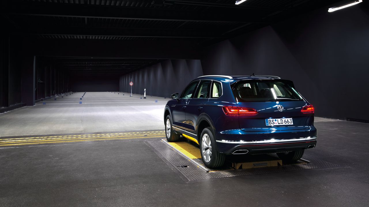 Lighting systems | High Beam Assist A parked dark blue Volkswagen SUV with its headlights switched on in a minimally illuminated empty building.