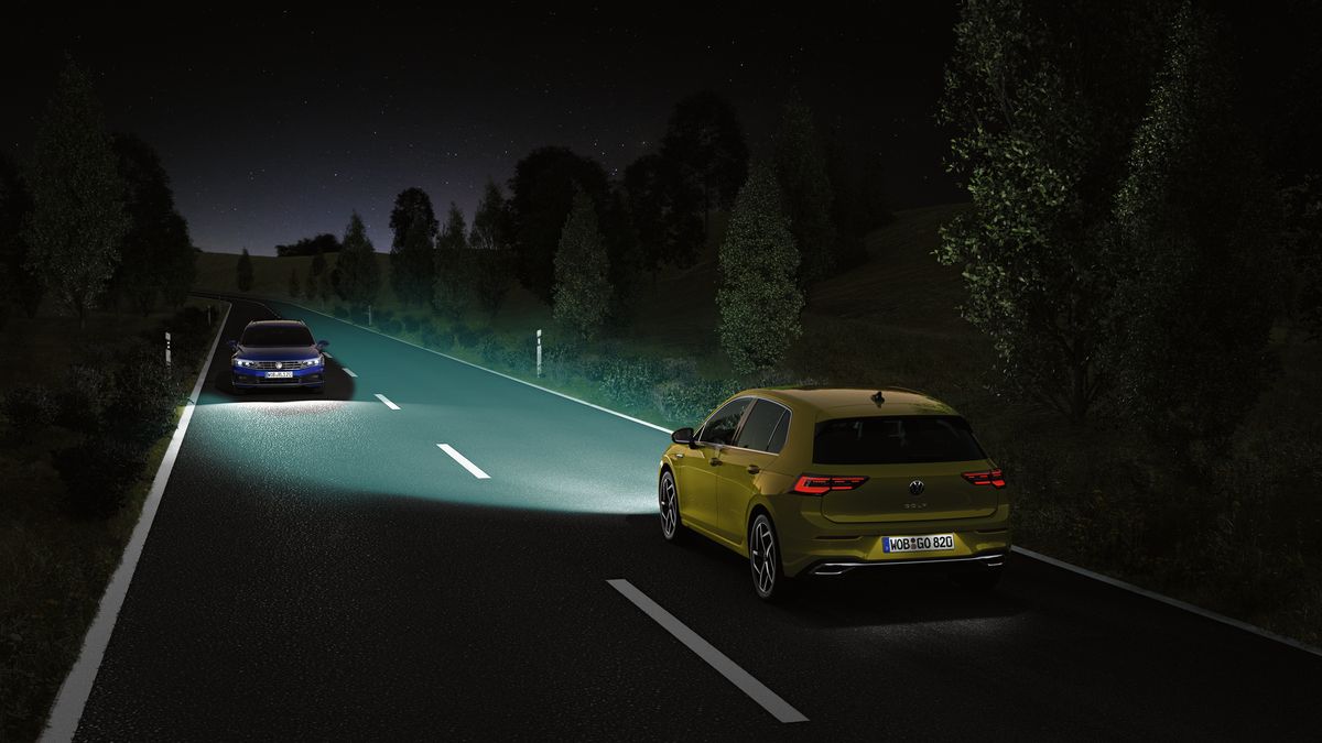 Lighting systems | Automatic headlight range control An image of a yellow Volkswagen vehicle with its headlamps switched on with another incoming vehicle on an opposite direction of the road at night.