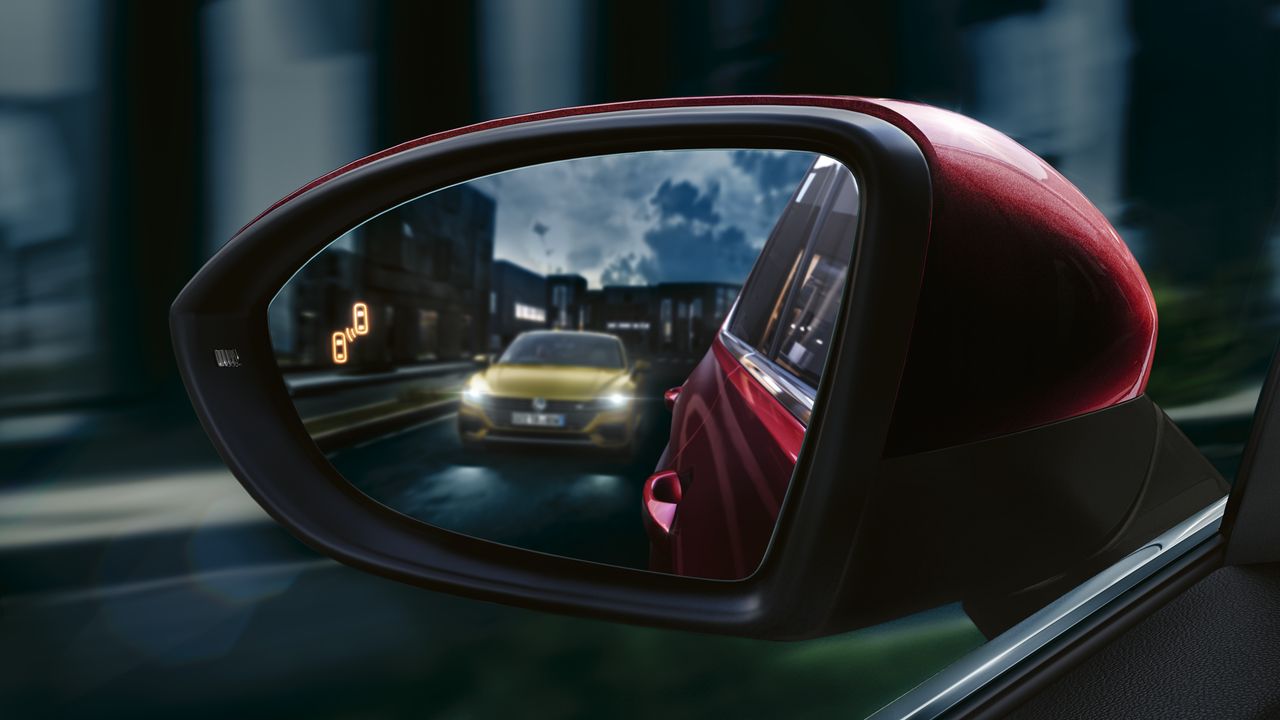 Electric door mirrors A close up image of a red Volkswagen vehicle's electric door mirrors with another vehicle in sight.