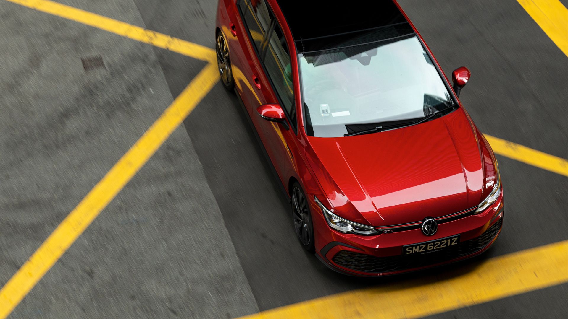Book a test drive An aerial view of a red Volkswagen GTI cruising past a road with yellow line markings.